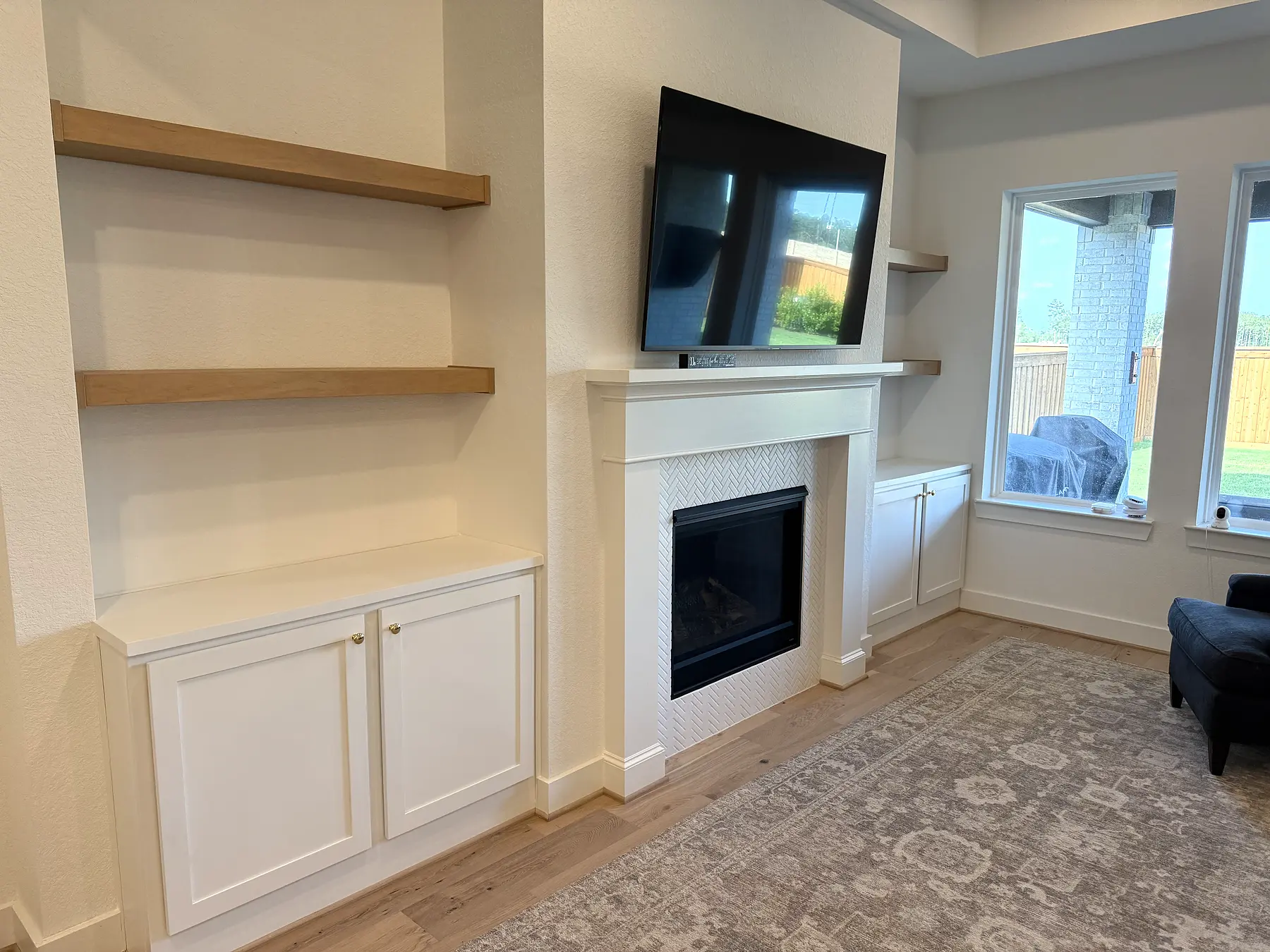 Completed fireplace built-ins with white base cabinets and natural wood floating shelves